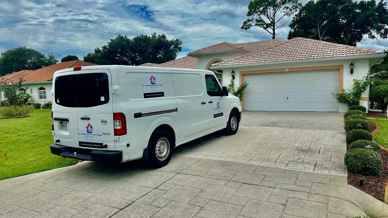 A white service van parked in the driveway of a residential home with a tiled roof and a two-car garage.