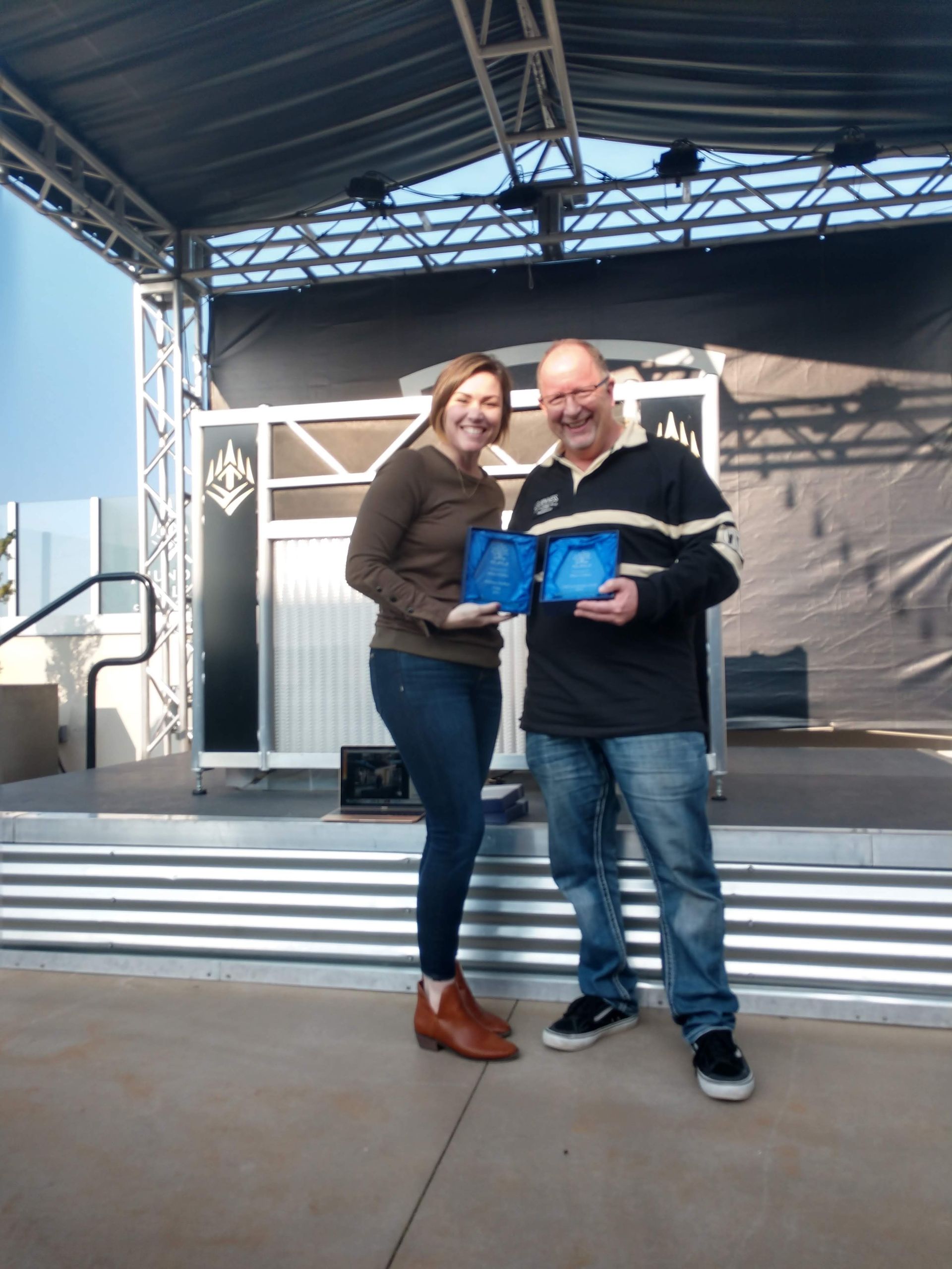 A man and a woman are standing on a stage holding blue boxes