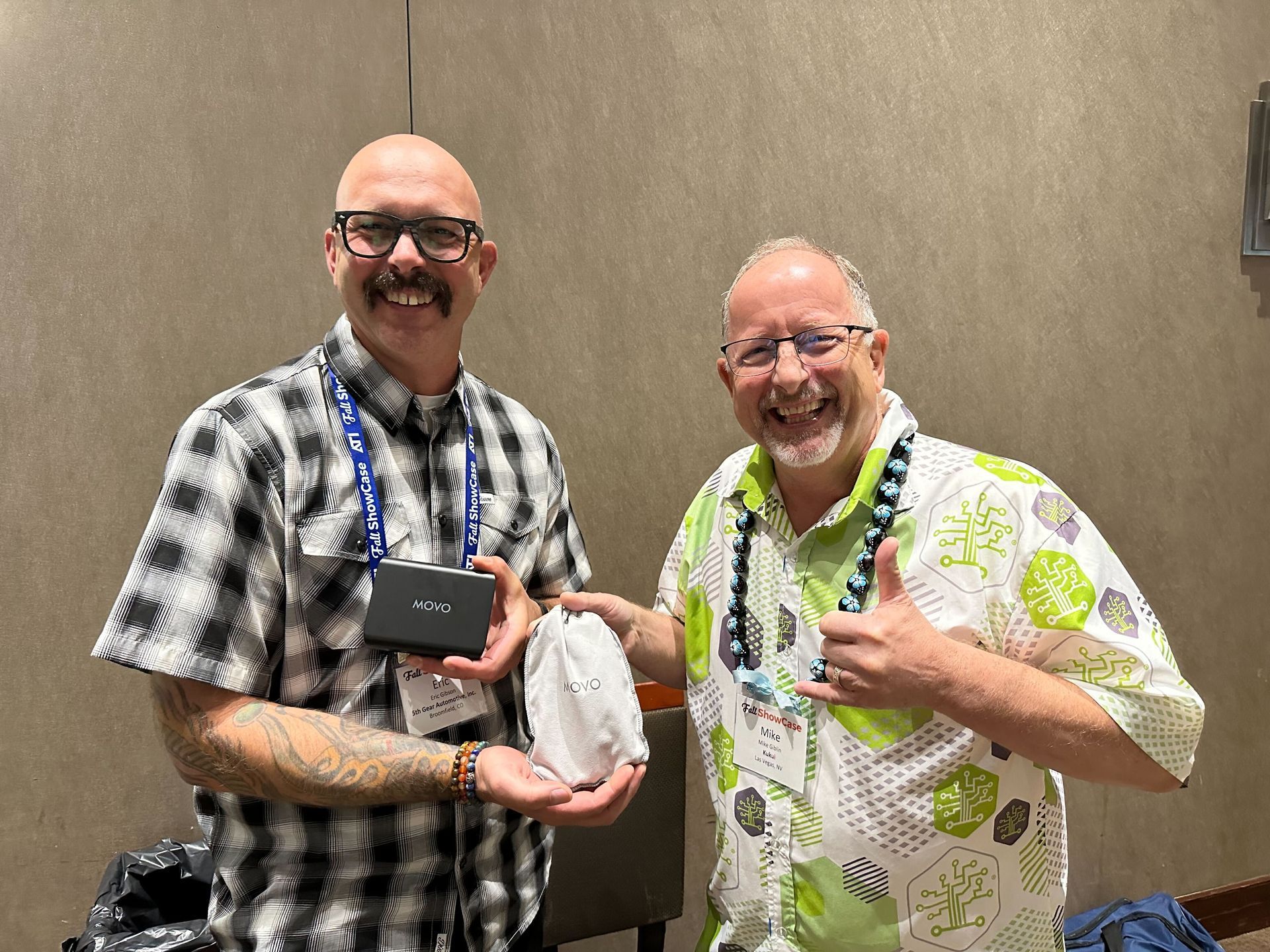 Two men are standing next to each other in a room . one of the men is giving the other a thumbs up.