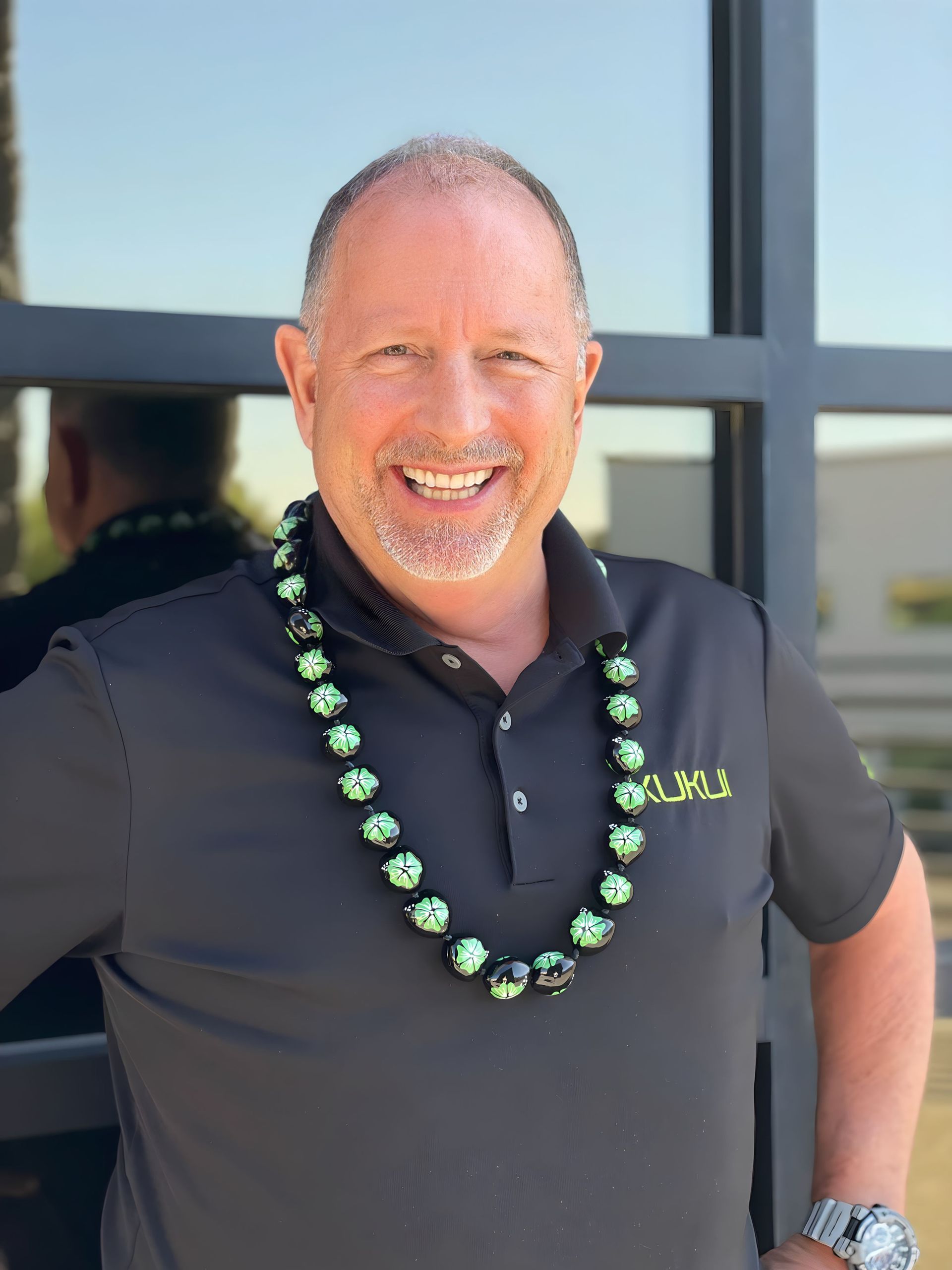 A man wearing a lei is smiling and standing in front of a building.