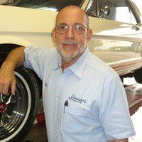 A man with a beard and glasses is leaning on the wheel of a car.