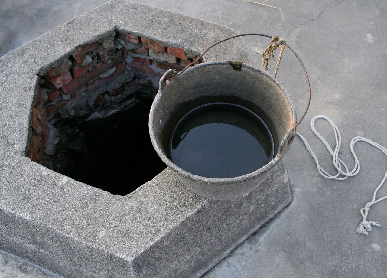 A bucket of water sits next to a hole in the ground