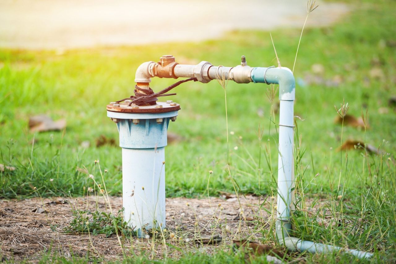 A water pump is sitting in the middle of a grassy field.