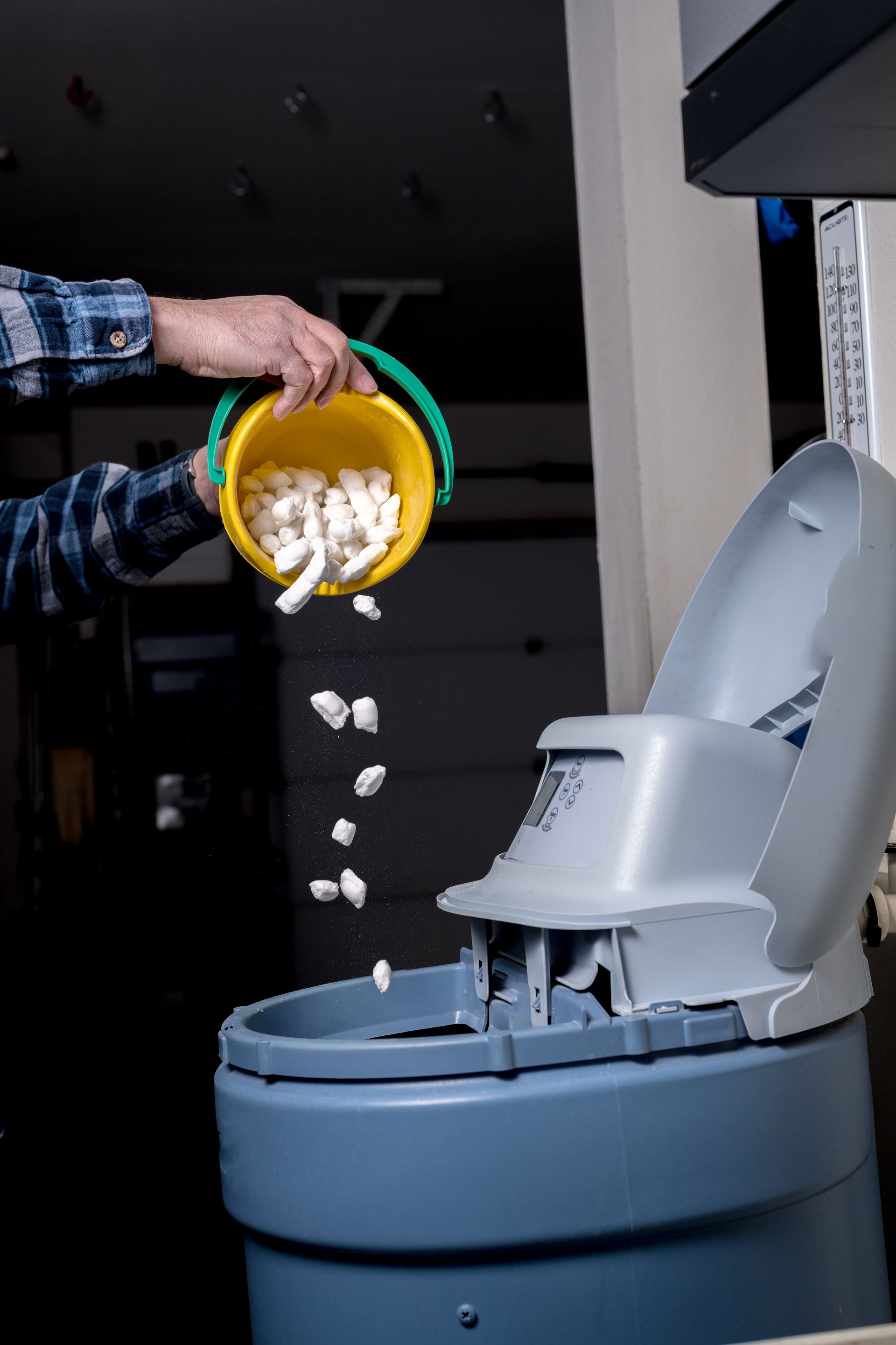 Man pours fresh salt from a yellow bucket into a water softener.