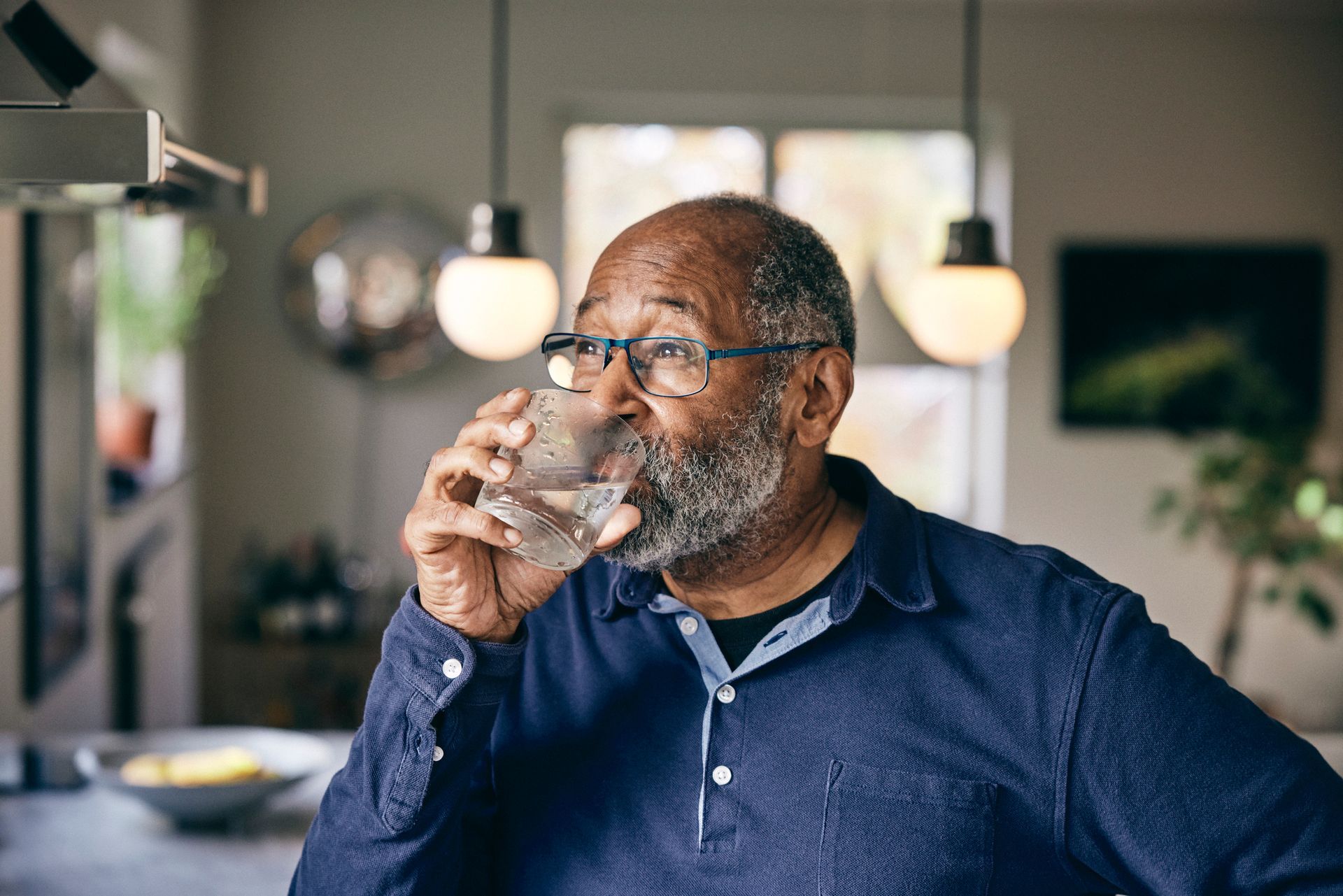 Contemplative senior man drinking water at home.