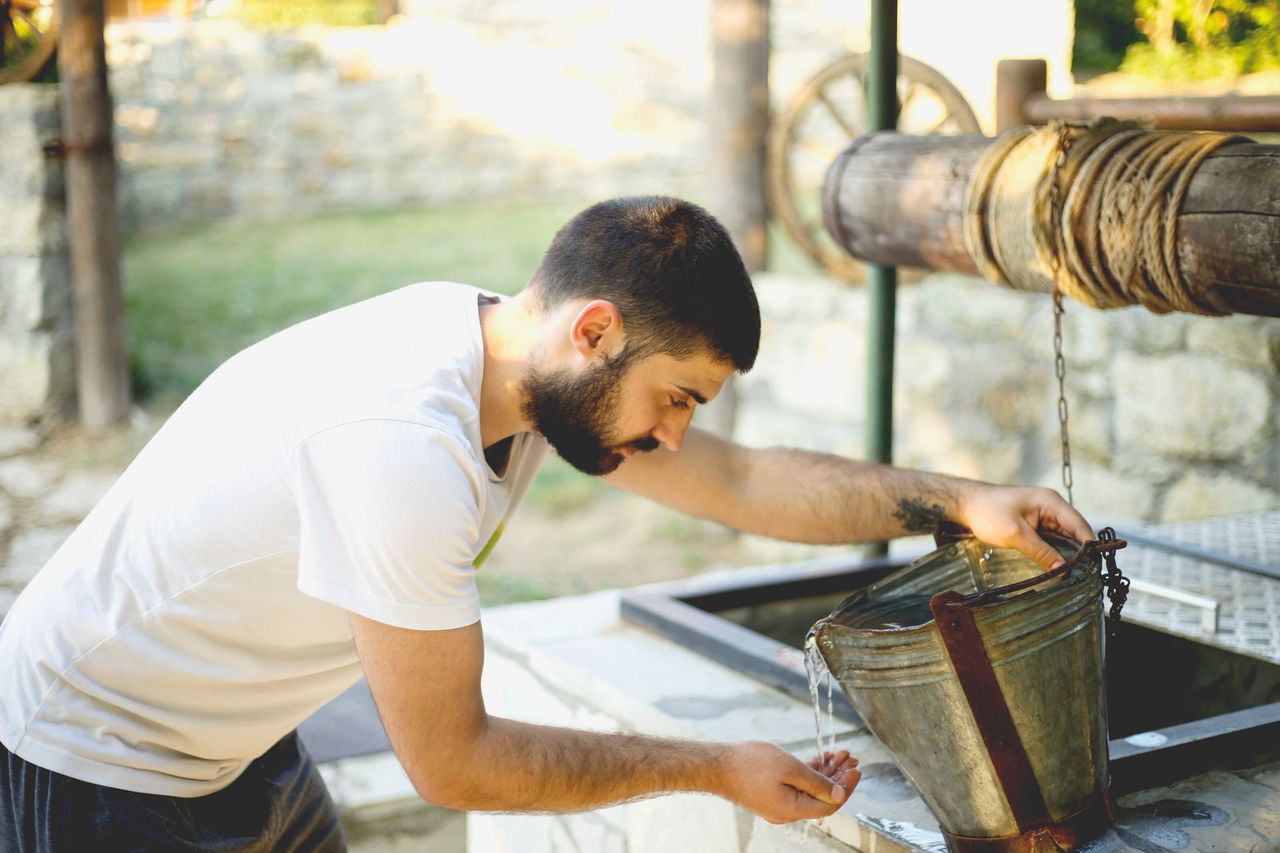 A young man drinking water from draw well.