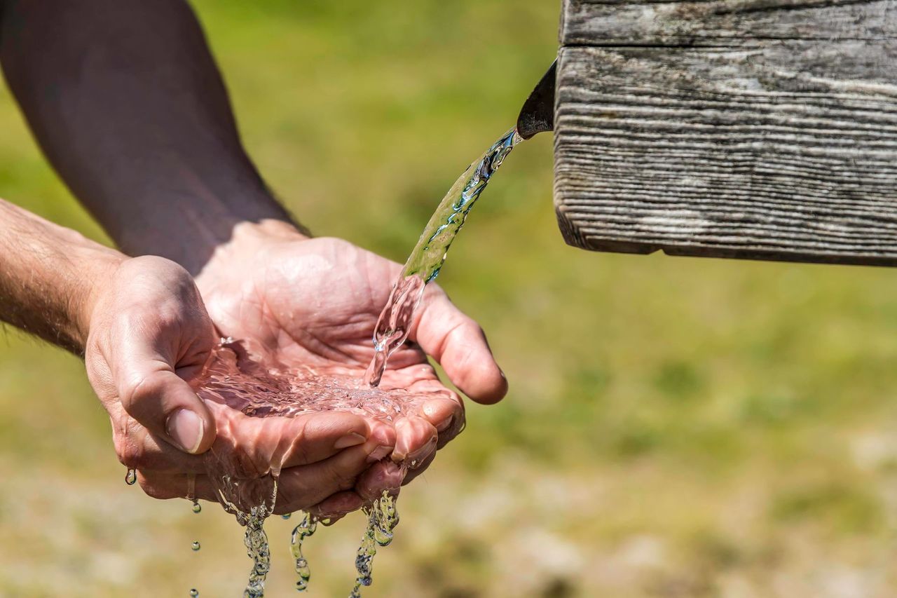A person is pouring water into their hands from a wooden fountain.