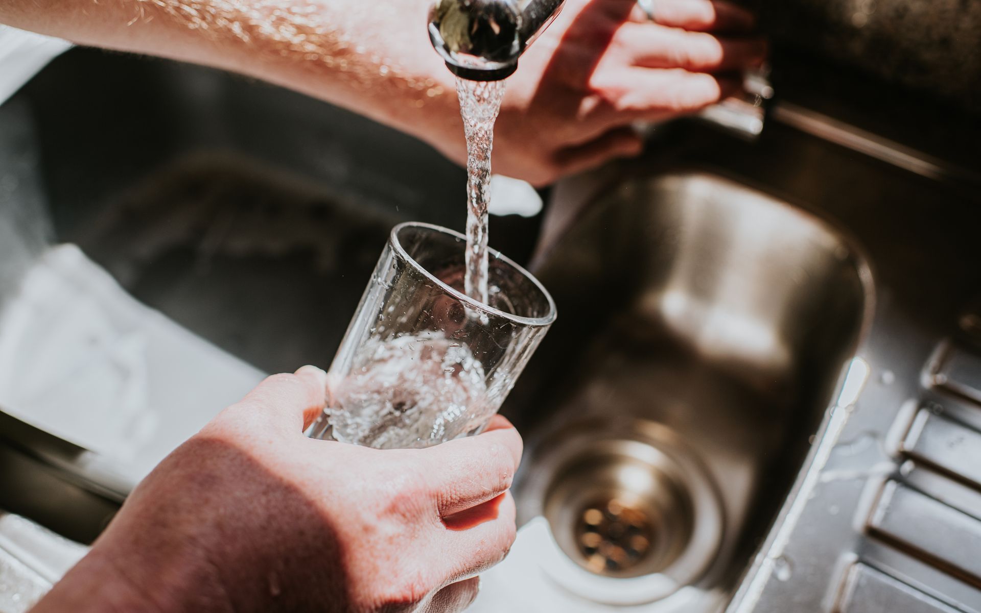 Close-up of a man turning a tap on in a kitchen.