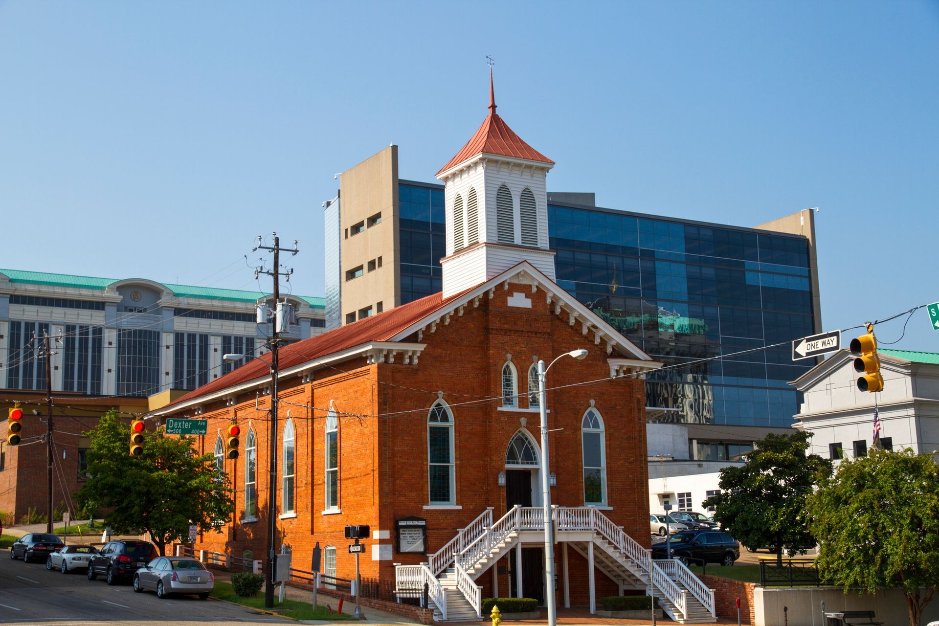A brick church with stairs leading up to it is in front of a large building.