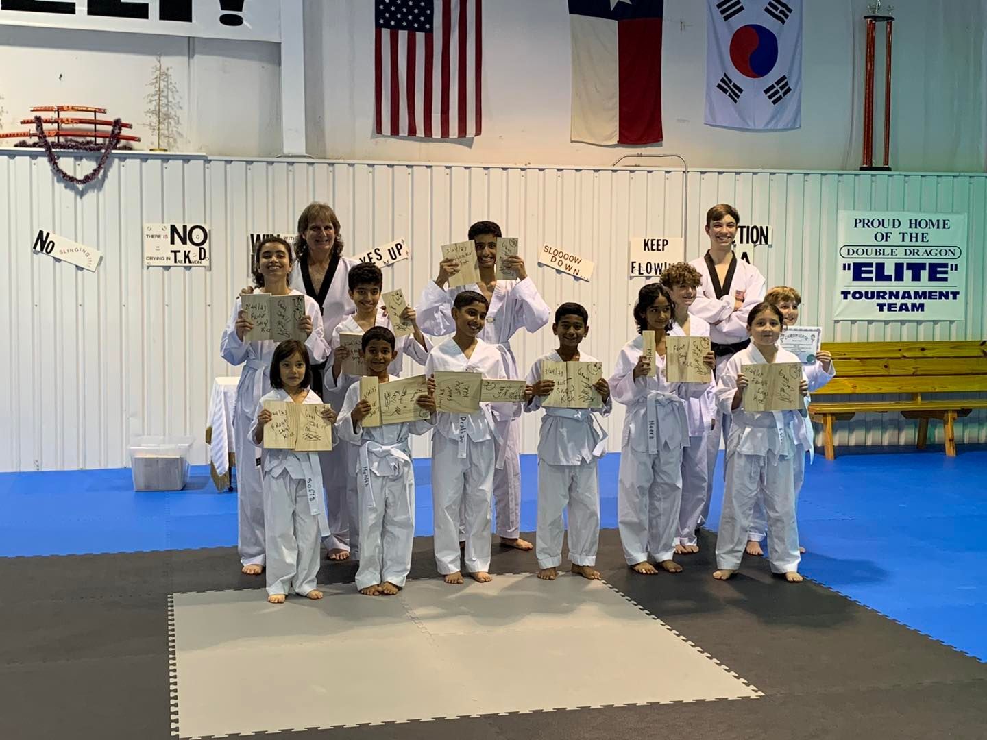 A group of children are standing on a blue mat holding certificates.