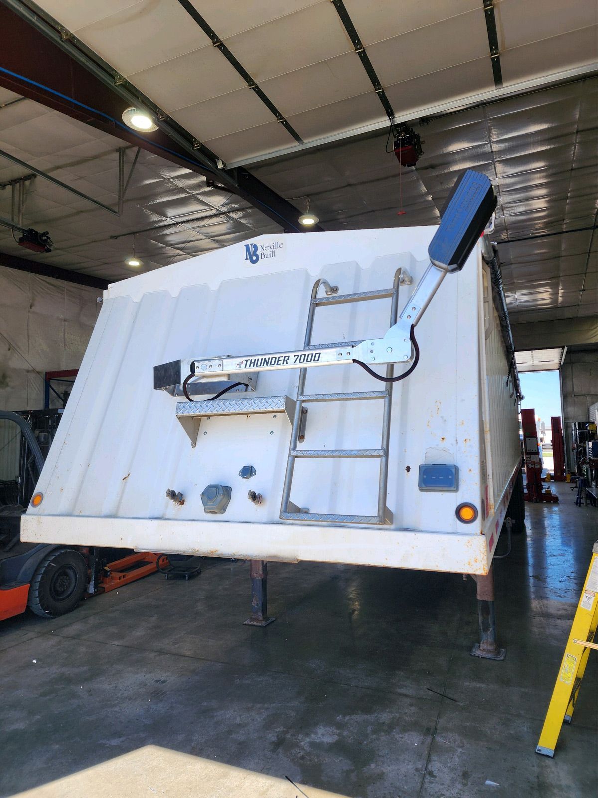 A white truck with a ladder attached to the back is parked in a garage.