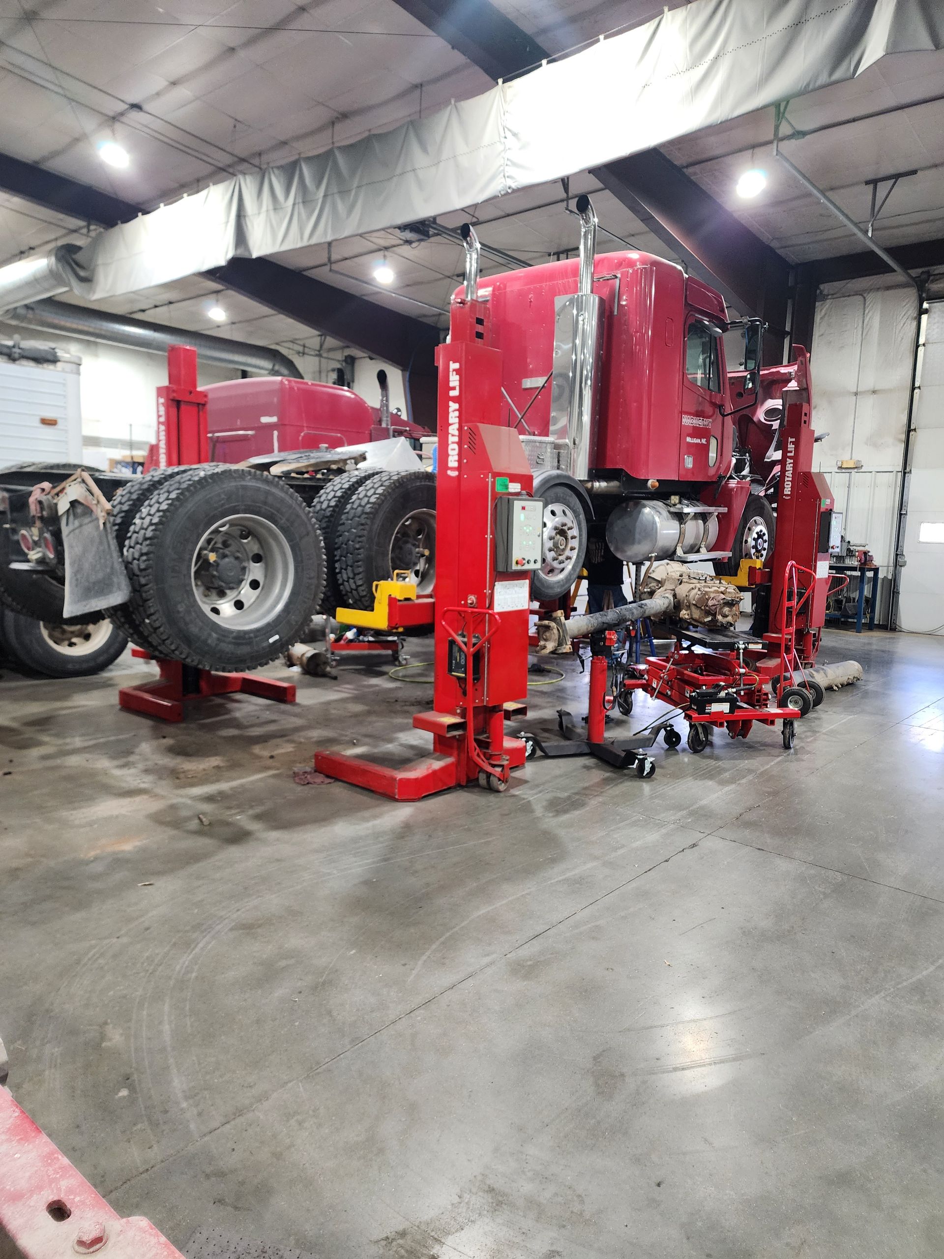 A red semi truck is sitting on a lift in a garage.