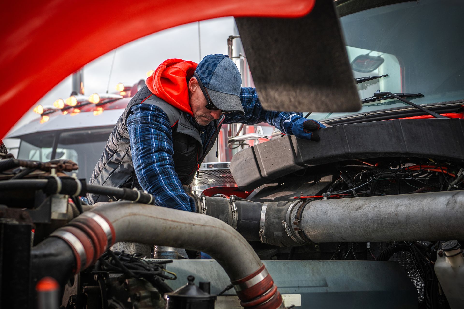 Mechanic checks engine in heavy truck during overcast day.