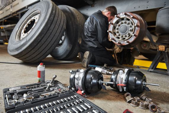 Truck repair shop technician servicing heavy-duty truck brakes with professional tools. Truck repair shop technician servicing heavy-duty truck brakes with professional tools.