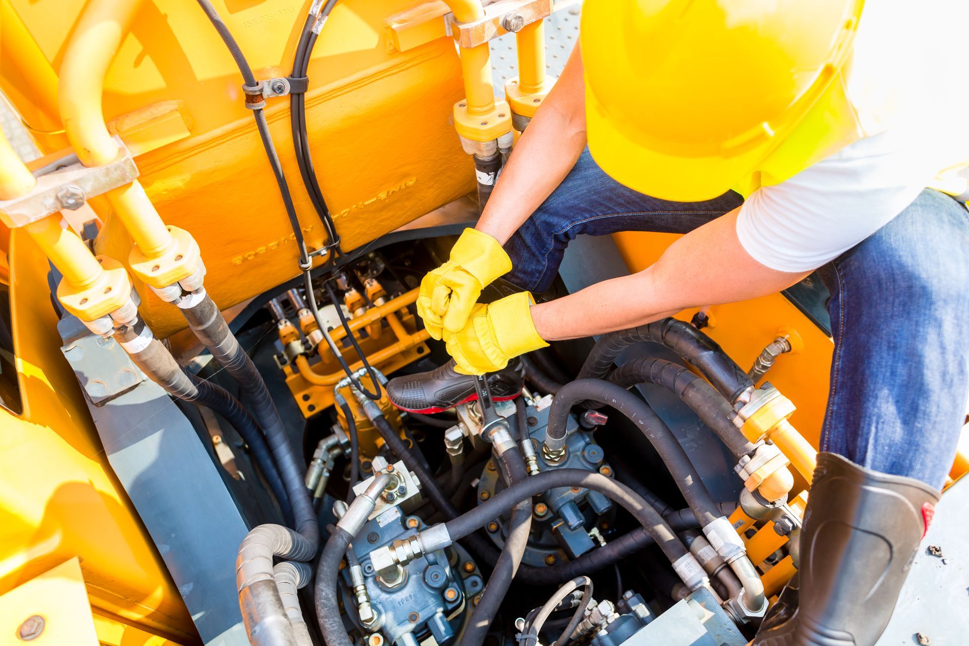 A worker performing maintenance on complex machinery with multiple black hoses.