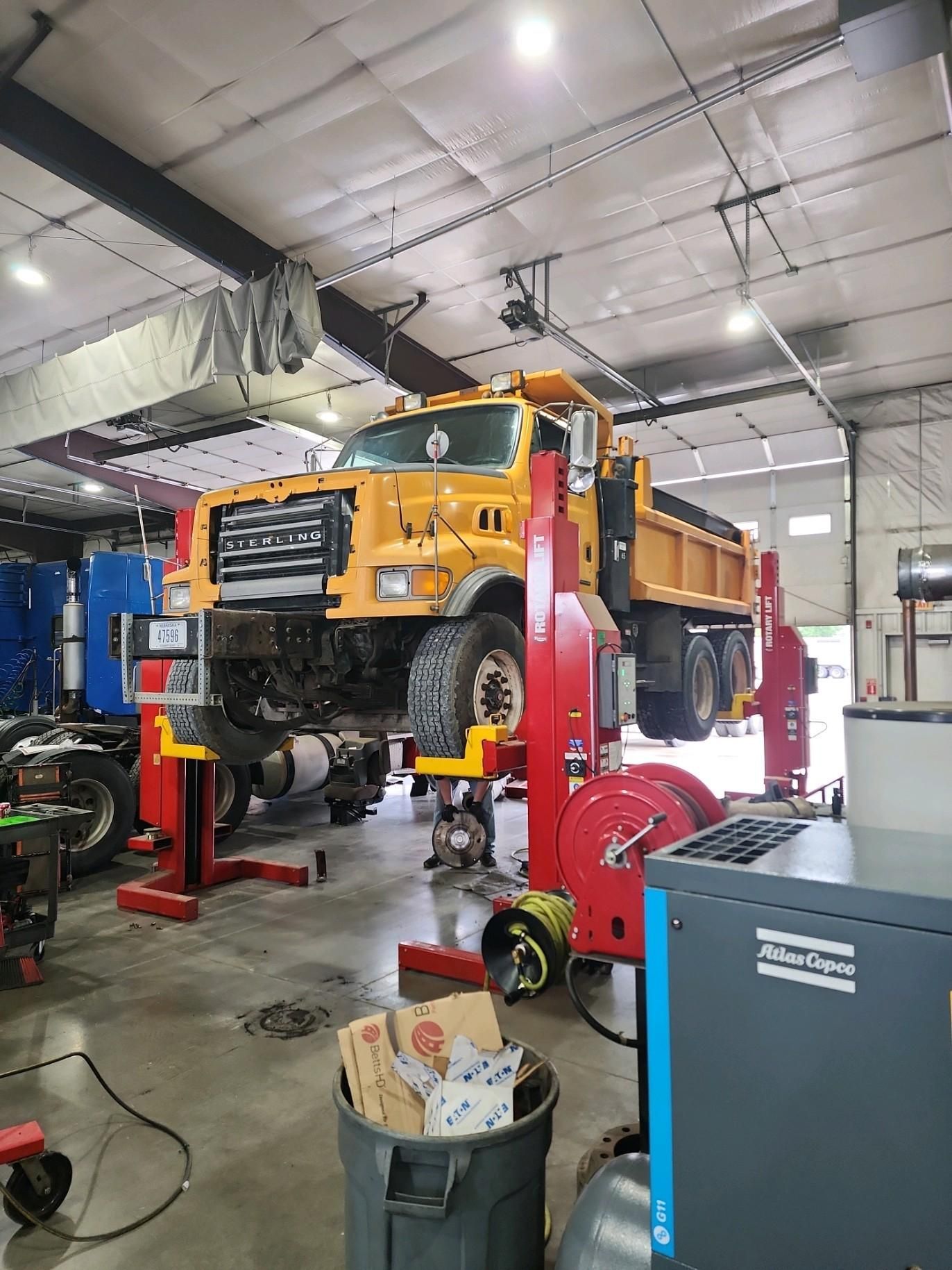 A yellow dump truck is sitting on a lift in a garage.