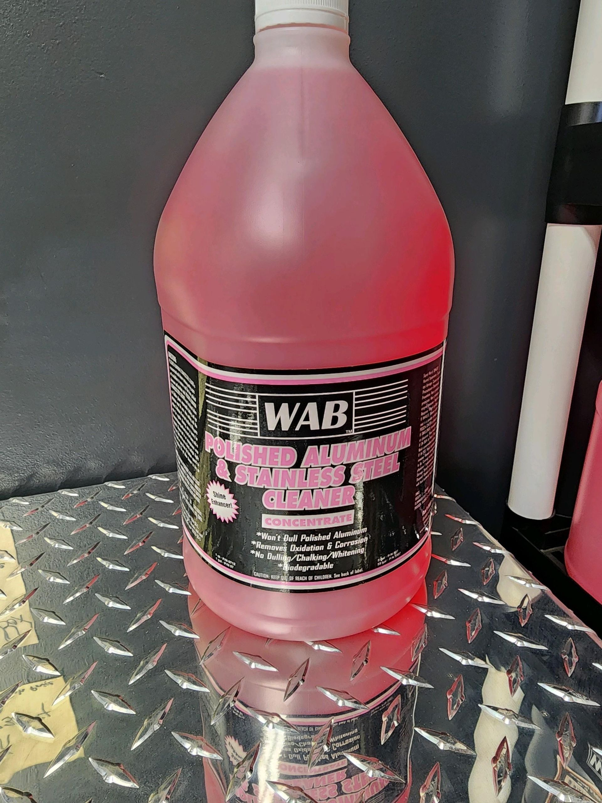 A bottle of wab pink liquid is sitting on a metal surface.