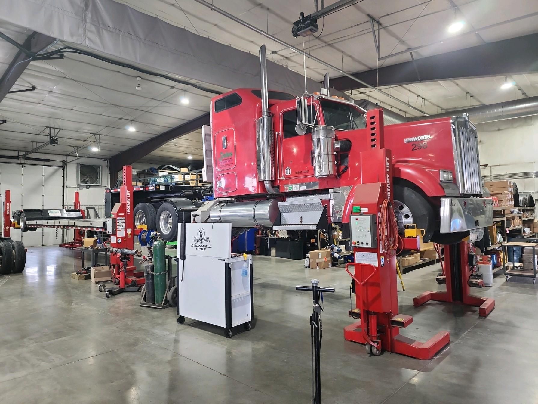 A red semi truck is sitting on a lift in a garage.