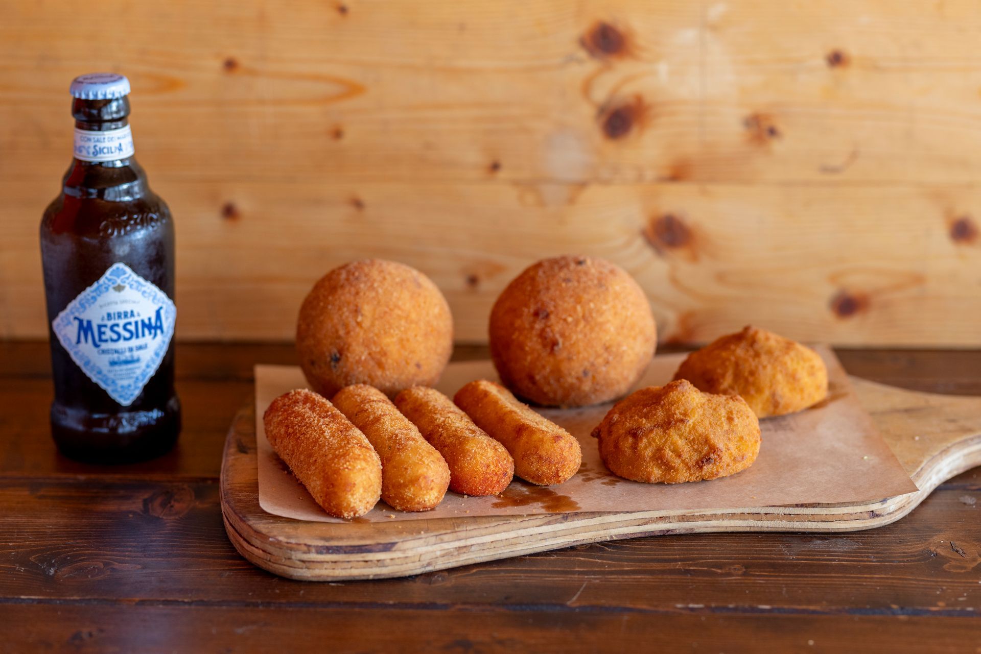 Un tagliere di legno con sopra del cibo fritto e una bottiglia di birra.