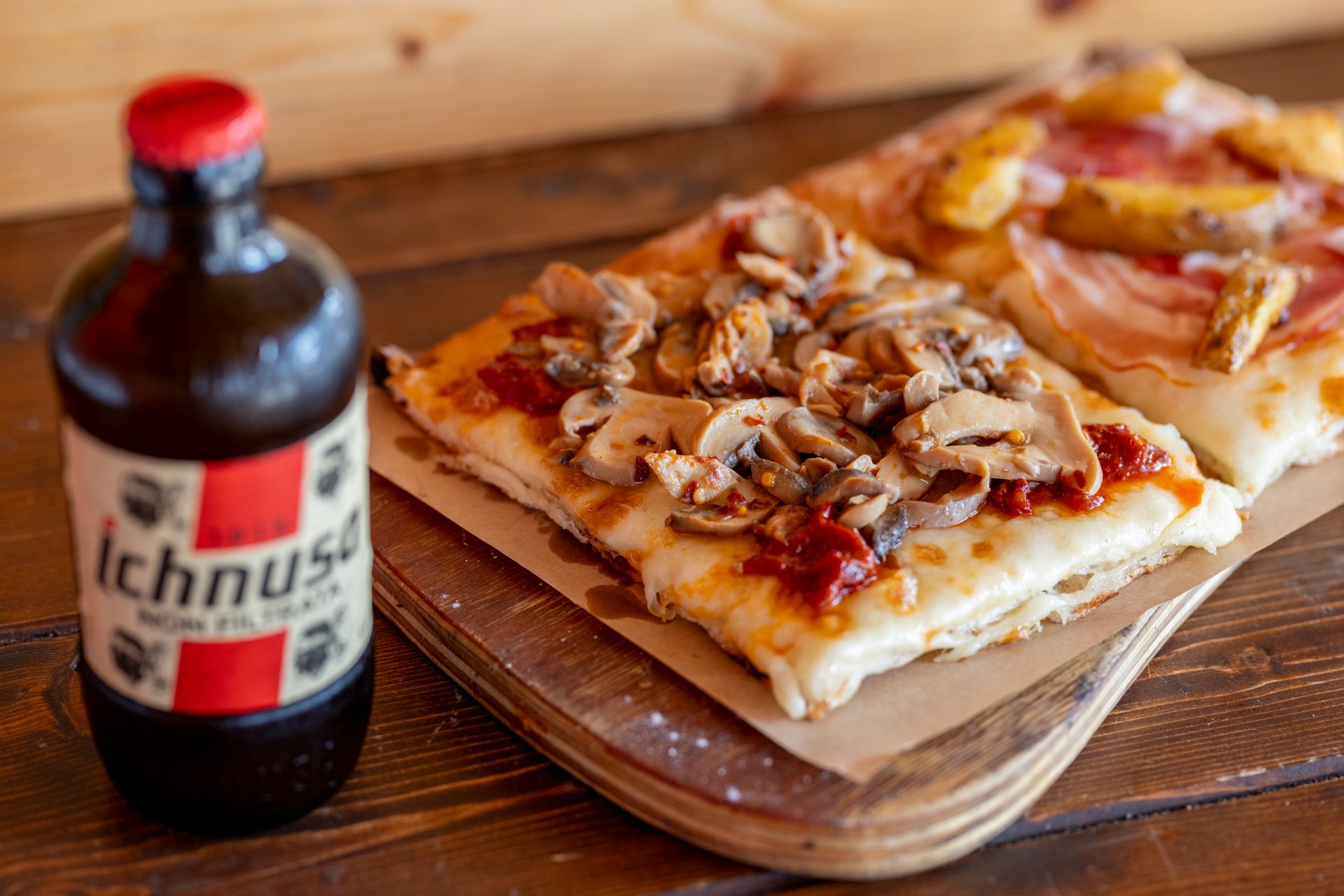 Una bottiglia di birra Ichnusa è accanto a una pizza su un tagliere.