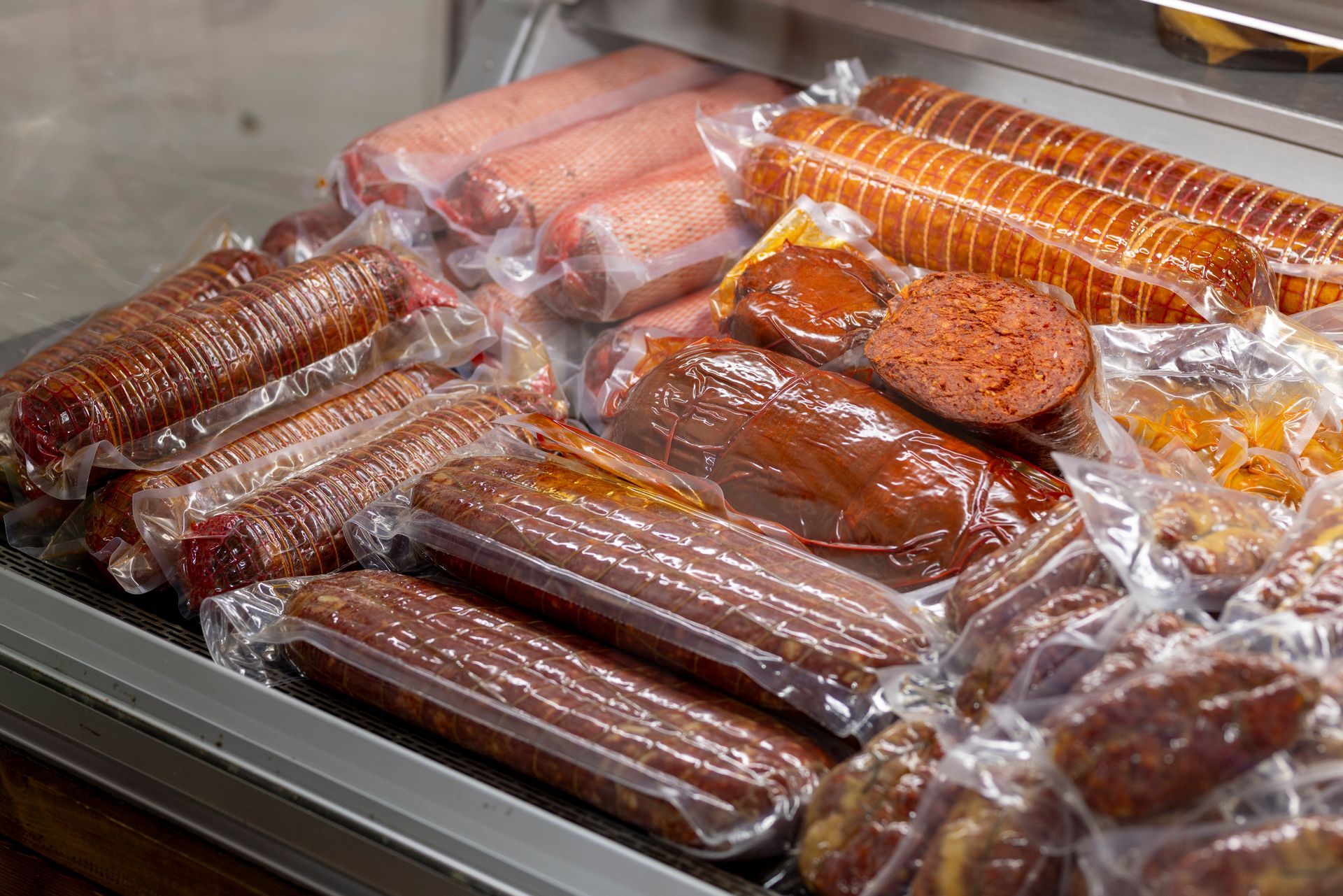 Una varietà di salsicce vengono avvolte nella plastica in un frigorifero.