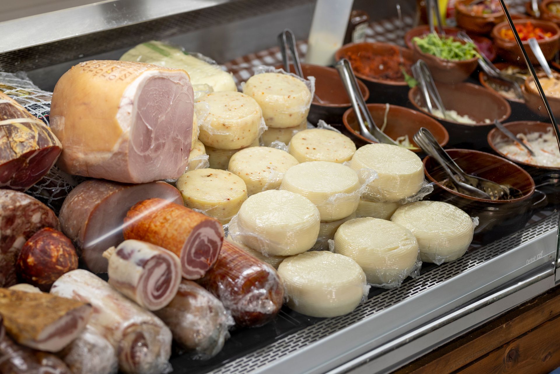 Una vetrina piena di salumi e formaggi di vario tipo.