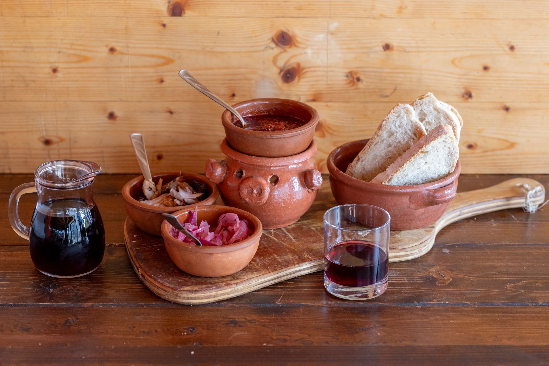 Un tavolo di legno sormontato da ciotole di cibo e un bicchiere di vino.