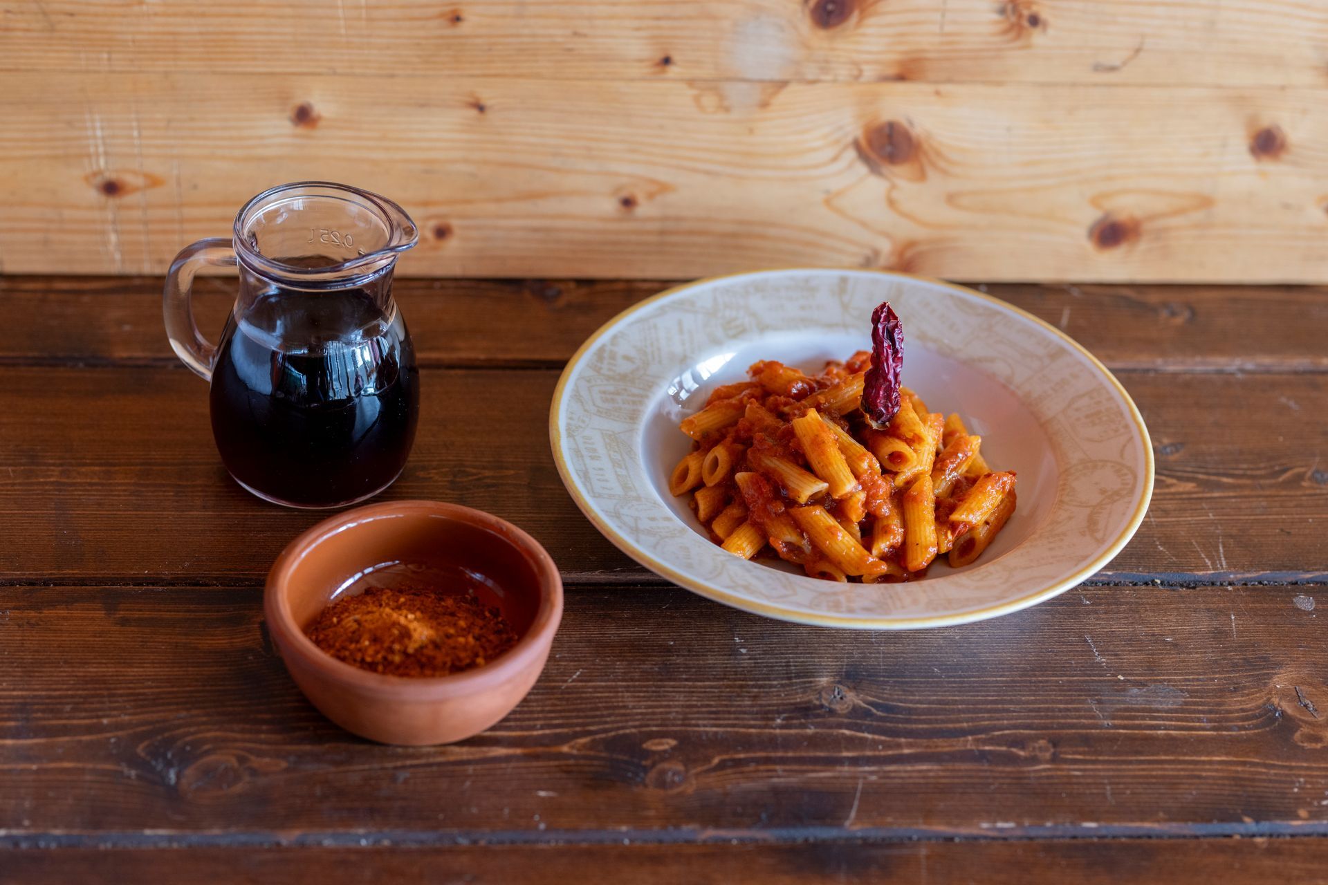 Un piatto di pasta con sugo e una brocca di sugo su un tavolo di legno.