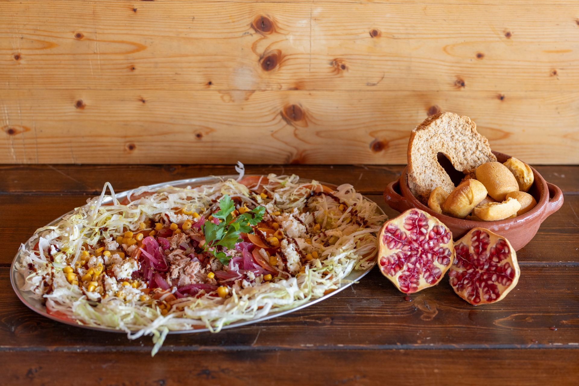 Un piatto di cibo è appoggiato su un tavolo di legno accanto a una ciotola di cracker e un melograno.