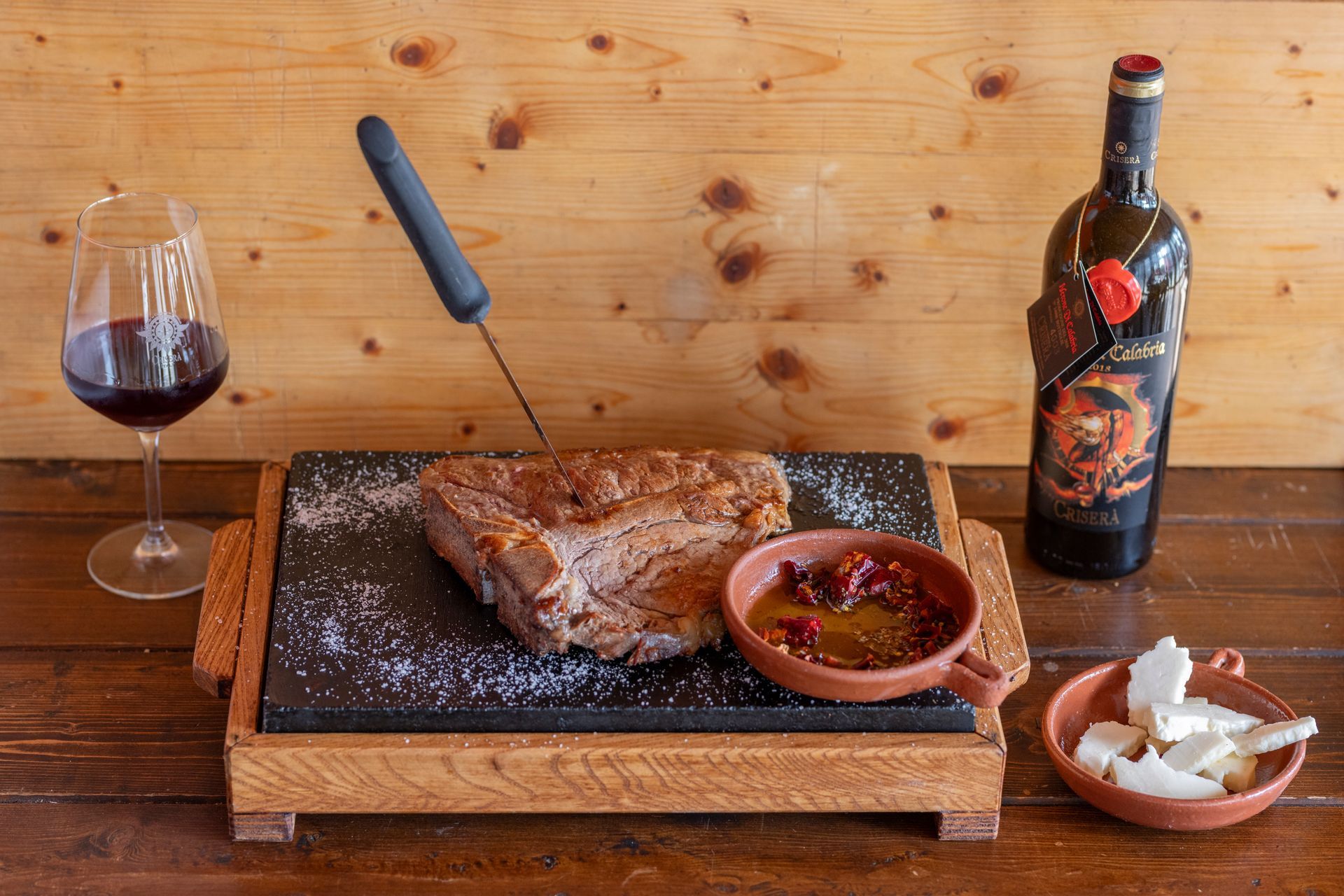 Una bottiglia di vino, un piatto di cibo e un bicchiere di vino sono su un tavolo di legno.