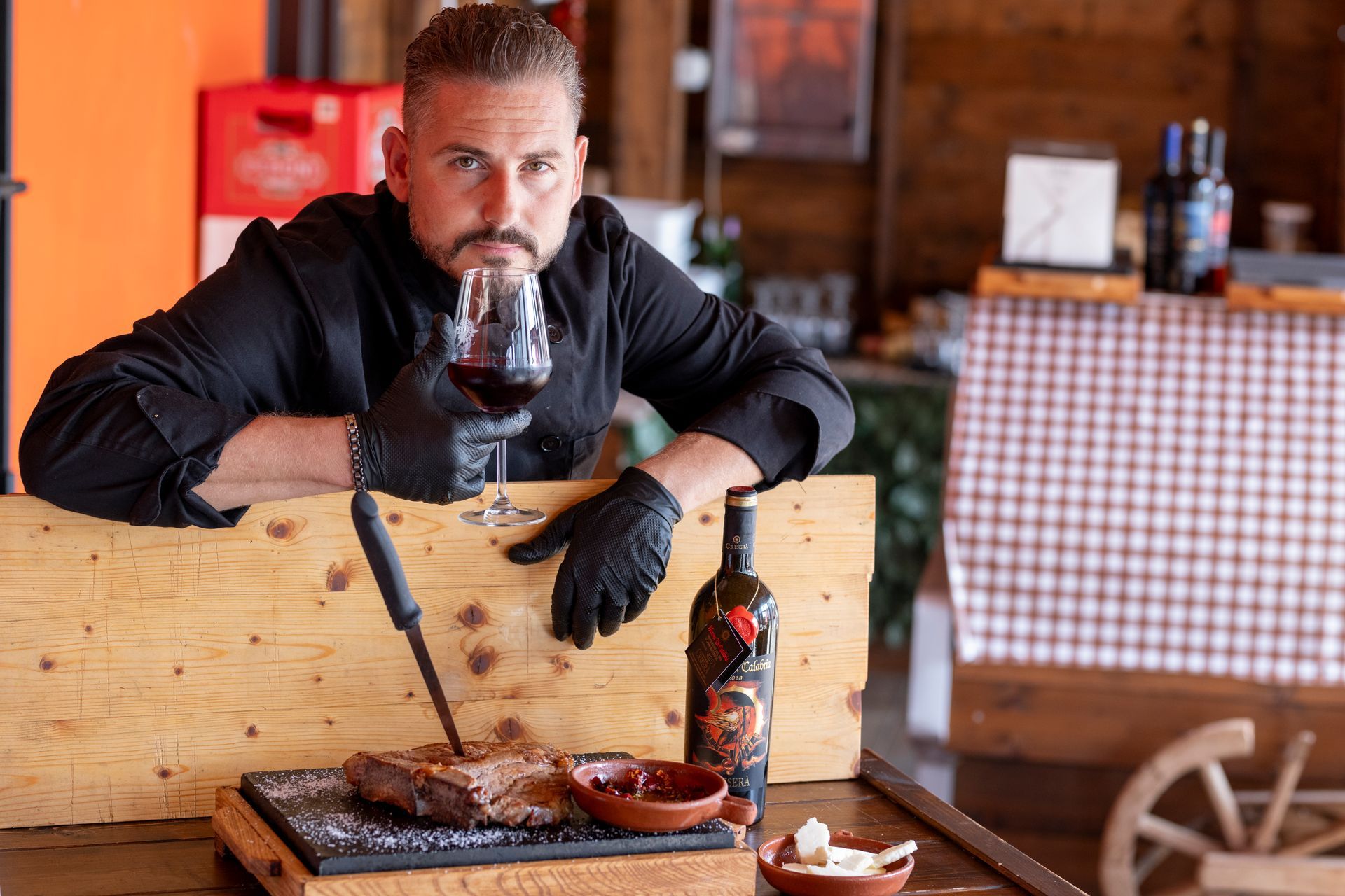 Un uomo tiene in mano un bicchiere di vino e taglia un pezzo di carne.