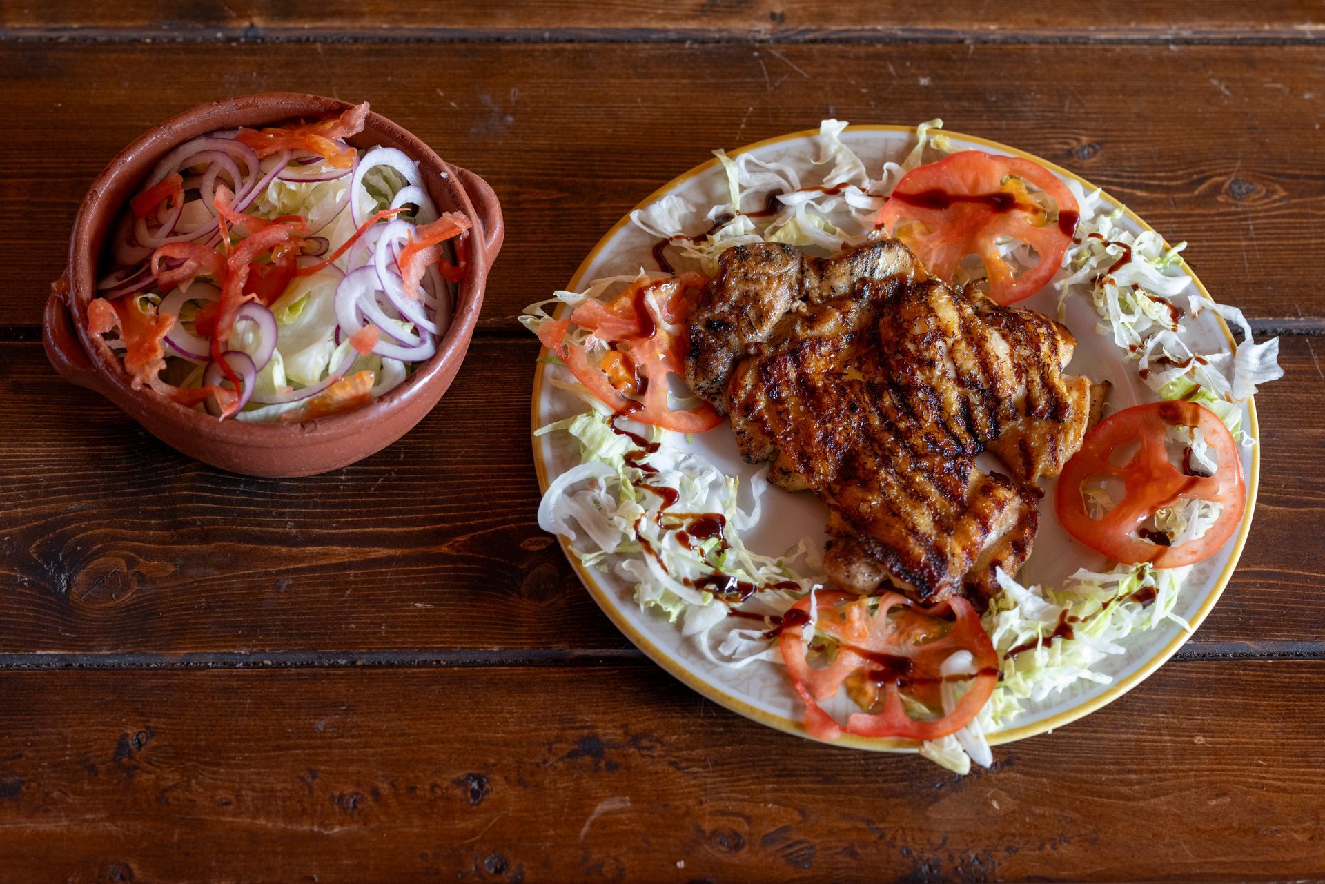 Un piatto di cibo e una ciotola di insalata sono su un tavolo di legno.