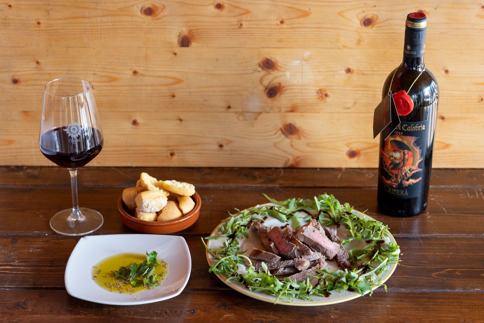 Una bottiglia di vino, un piatto di cibo e un bicchiere di vino sono su un tavolo di legno.