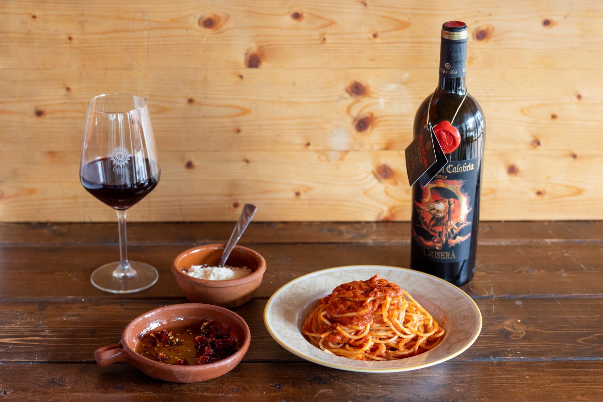 Una bottiglia di vino, un piatto di spaghetti e un bicchiere di vino sono su un tavolo di legno.