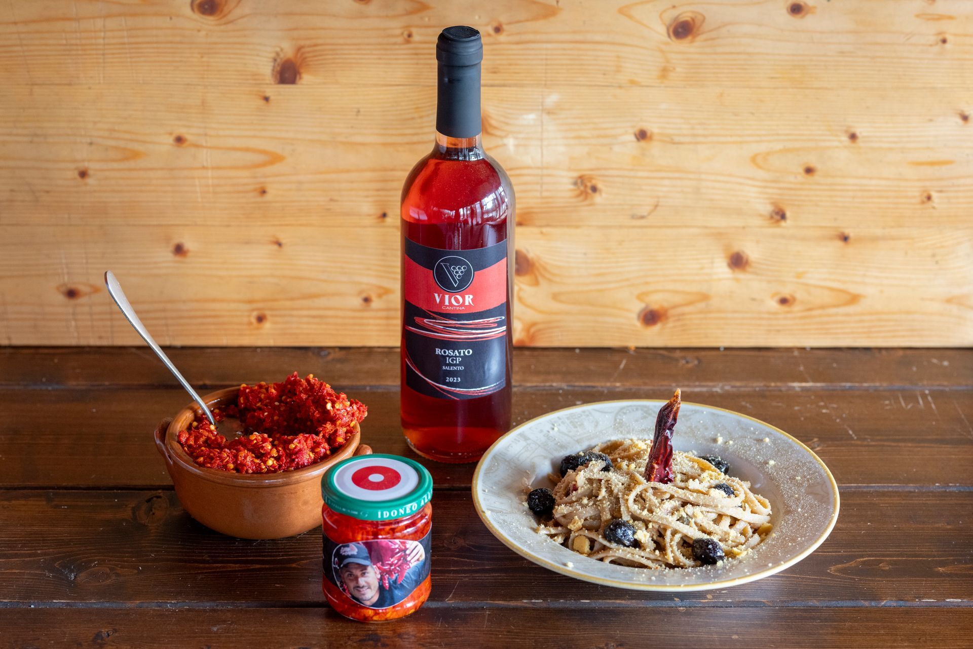Una bottiglia di vino, un barattolo di salsa e un piatto di pasta su un tavolo di legno.