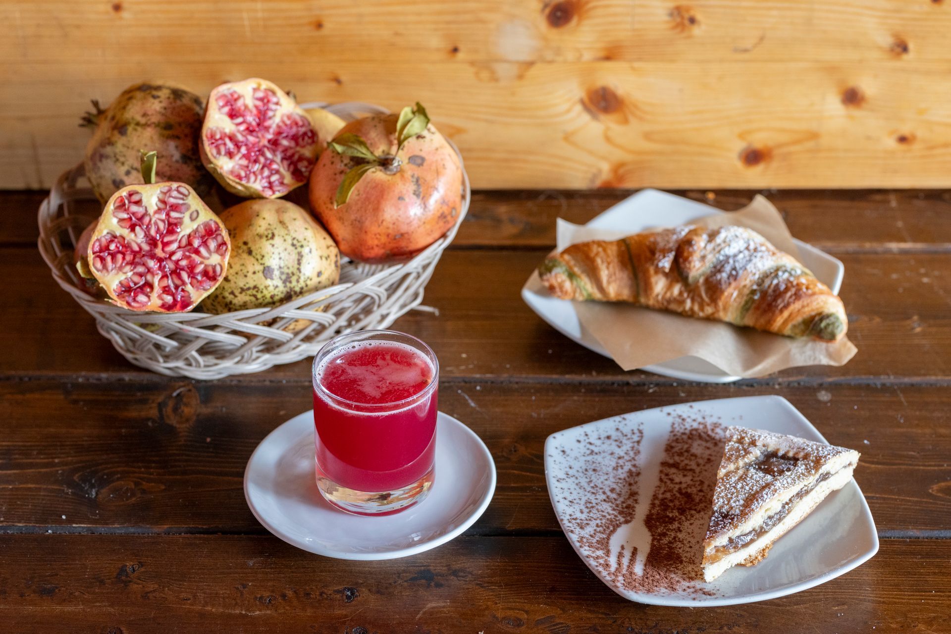 Un tavolo di legno sormontato da piatti di cibo e un cesto di melograni.