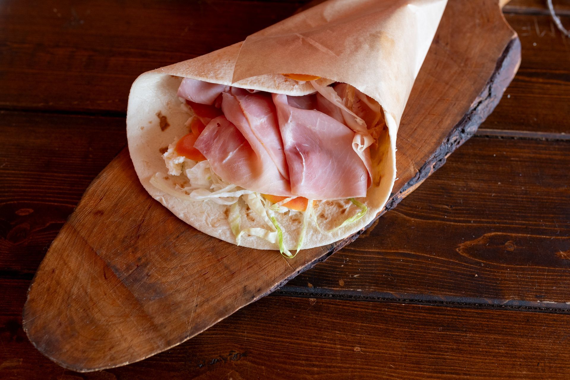 Una tortilla con prosciutto e verdure su un tagliere di legno.