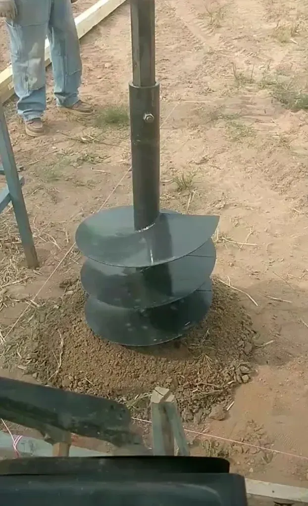 Auger drilling a hole in the ground; a person is nearby.