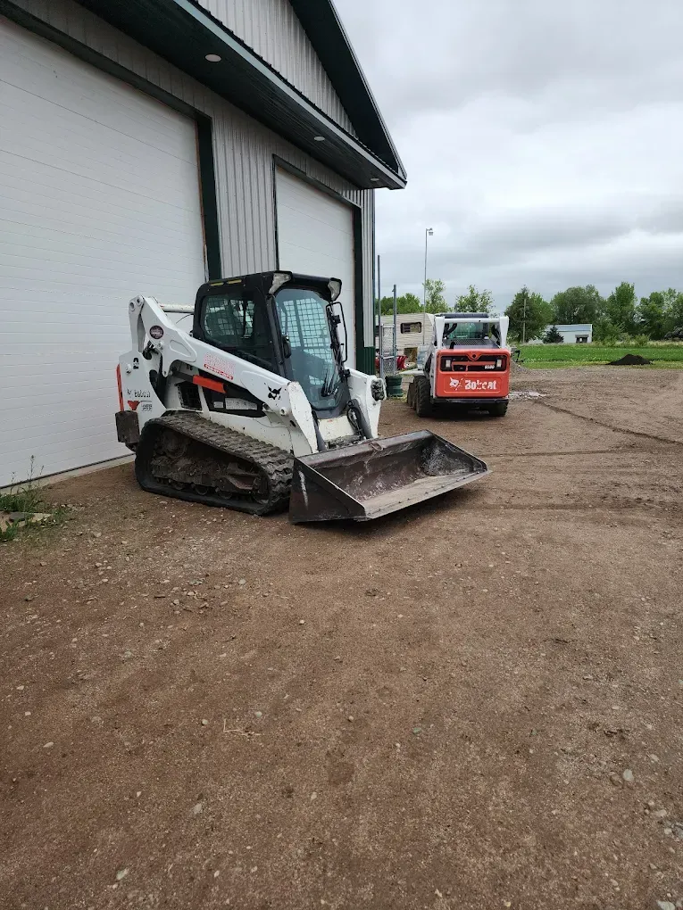 White Bobcat track loader parked outside a building with two garage doors.