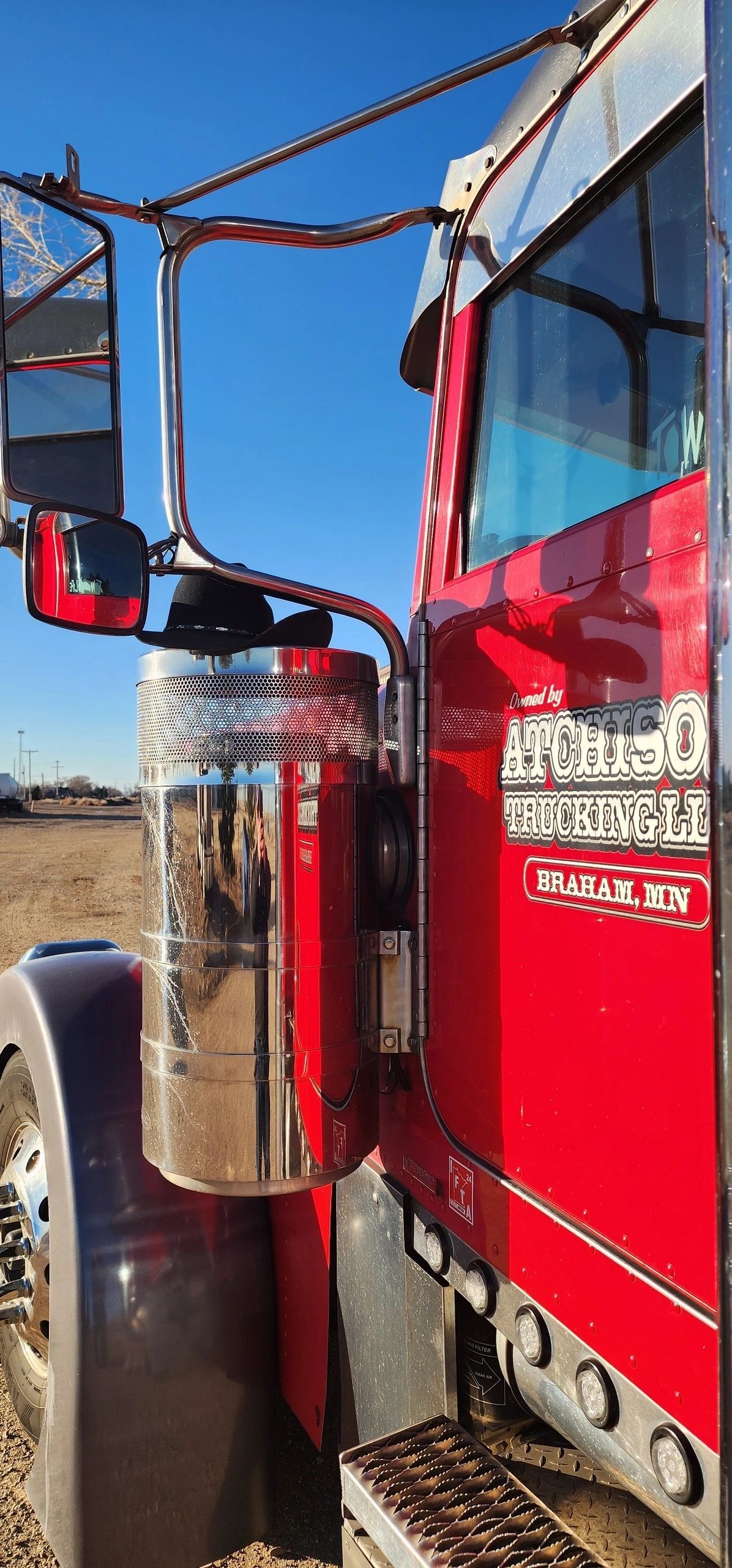 Side view of a red semi-truck with chrome details, parked outside on a sunny day.
