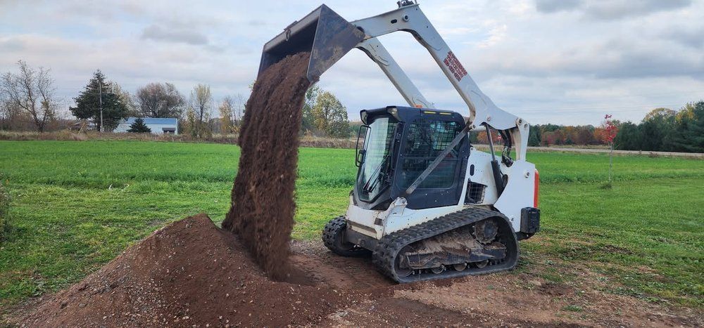 A white Bobcat skid steer dumping dirt onto a pile in a field. Cloudy sky.