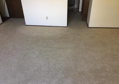 Tan carpet in a room with white walls, a doorway, and a hallway.