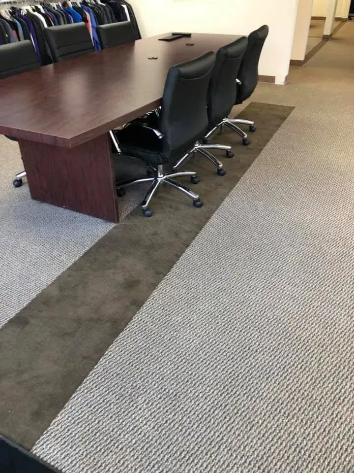 Conference room with a long table, black chairs, and a strip of darker carpet on a lighter carpet.