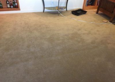 Tan carpeted floor with a few items along the wall: a table, a small box, and a wooden bookcase.