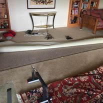 A room with rolled-up beige carpet revealing a rug and installation equipment. Furniture and decorations are visible.