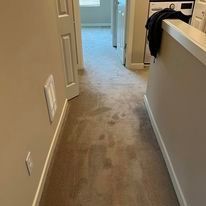 Hallway with stained beige carpet, open doorways, and a partially visible washing machine.