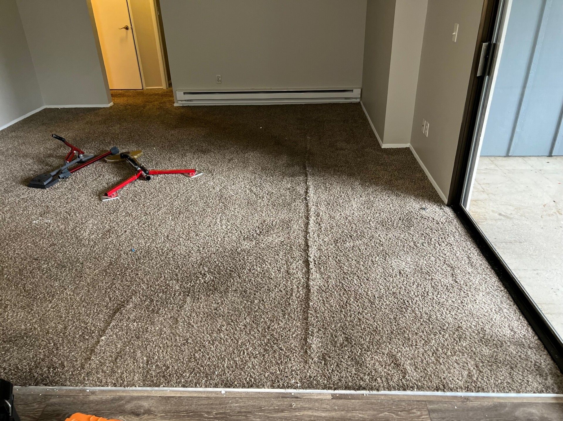 Room with carpet, a seam down the middle, and tools. Sliding glass door is on the right.