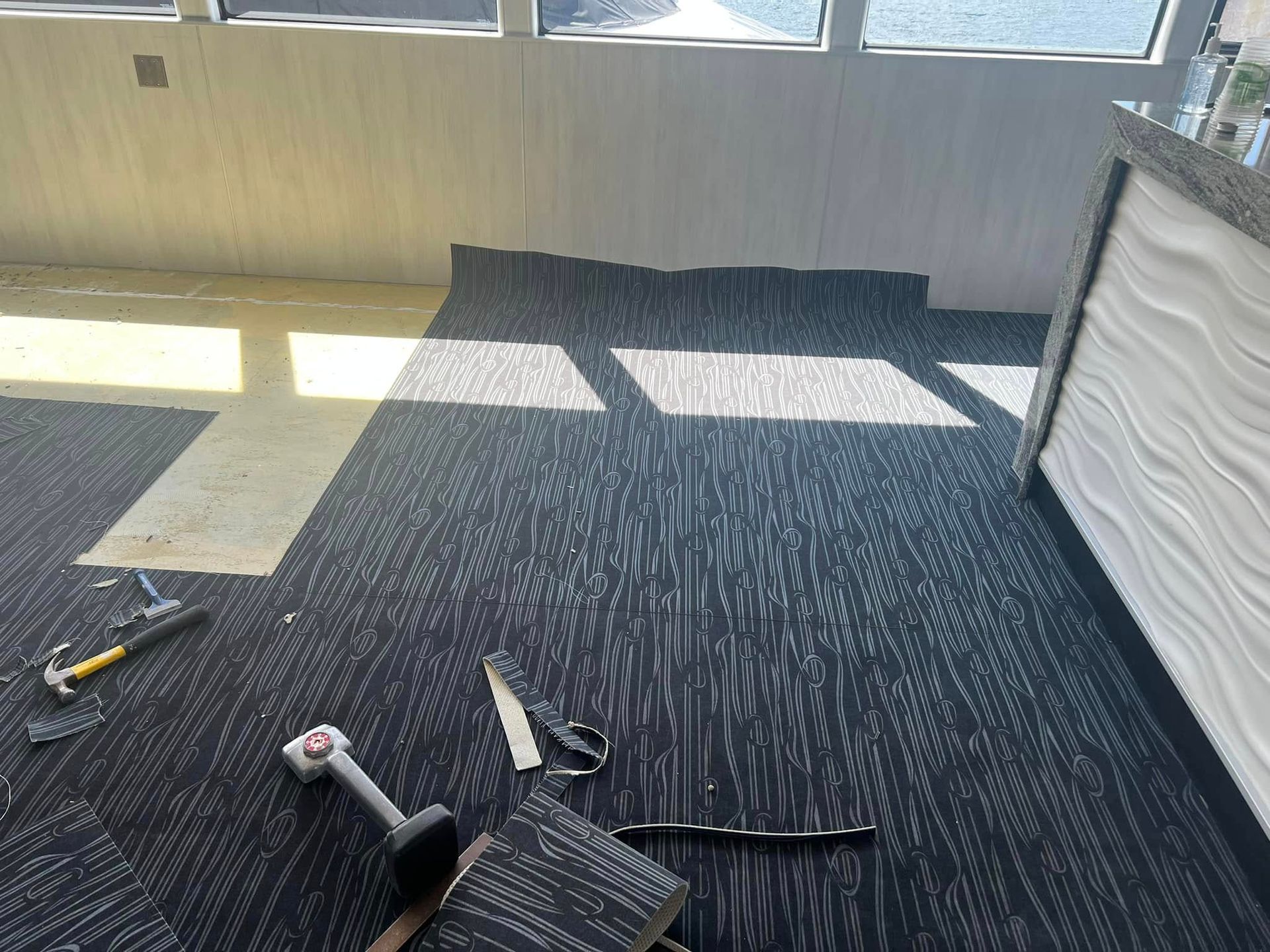 Installing carpet tiles in a room with white walls, sunlight, and tools.