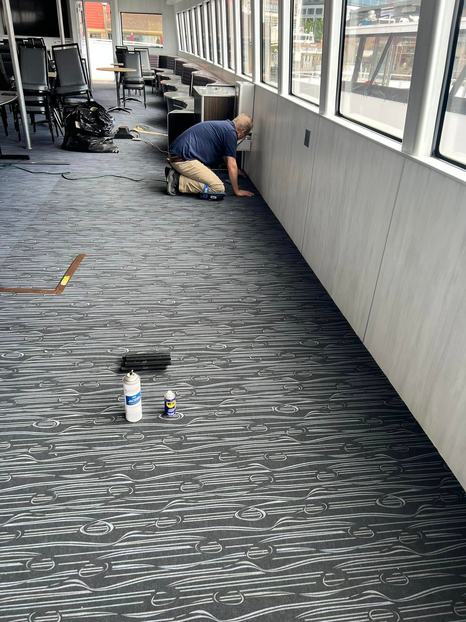 Man installing flooring in an interior space, kneeling near a wall and a window.