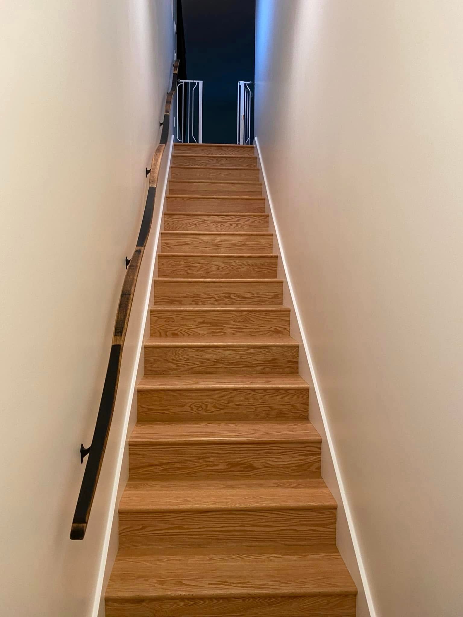 Wooden staircase with handrail and under-stair lighting, ascending to a dark opening.